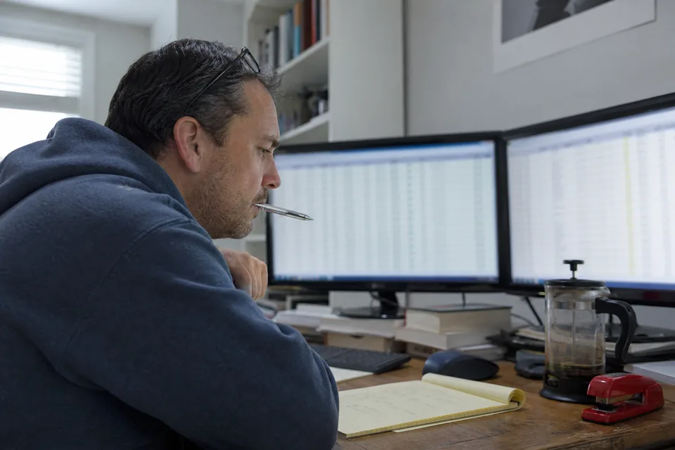 Domain investor at a desk with two monitors comparing a long list of names and prices