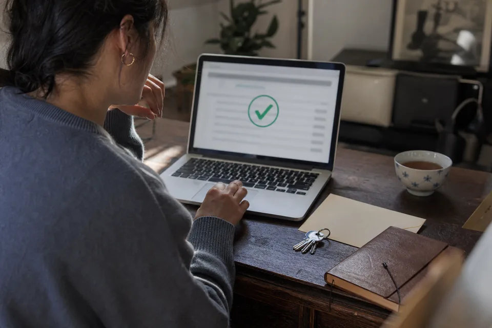 Laptop showing a payment confirmation with a green check next to keys and a notebook