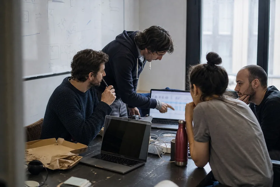 Early stage startup team of four around a table with laptops, working through a shortlist of names